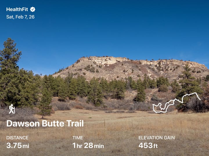 A image of Dawson Butte, tan rock standing above dry prairie grass and green pine trees, underneath a clear blue sky.